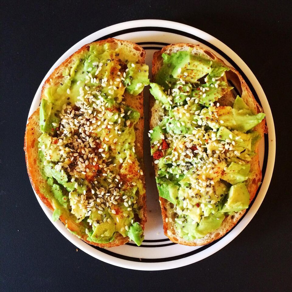 Ein gesundes Avocadotoast bestreut mit schwarzen und weißen Sesamsamen auf einem weißen Teller