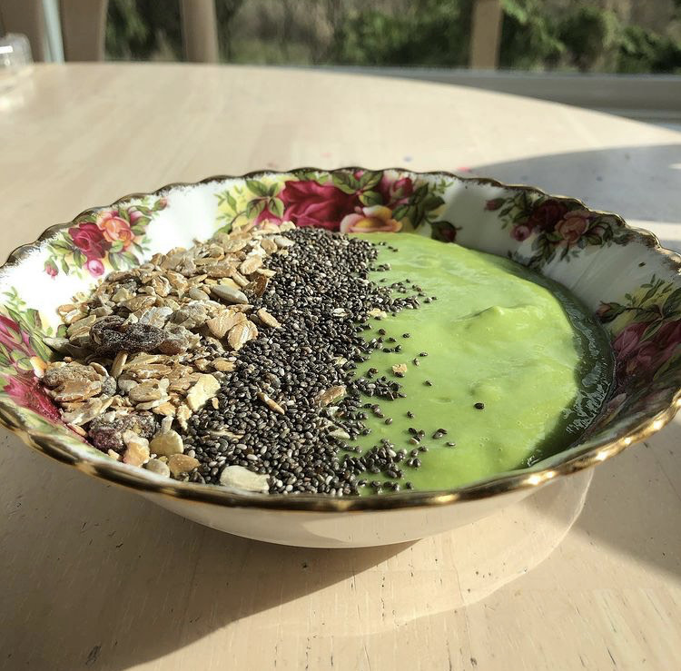 Eine grüne Smoothie-Bowl garniert mit Müsli und Chia-Samen